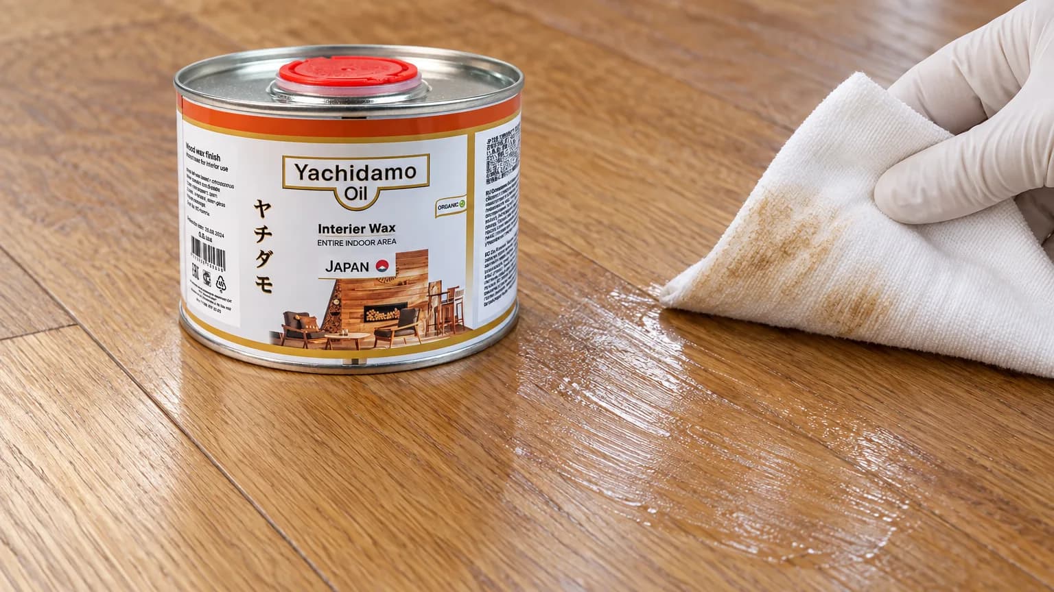 Банка Yachidamo Oil Interior Wax стоит на дубовом полу рядом с липким участком и белой салфеткой со следами покрытия.