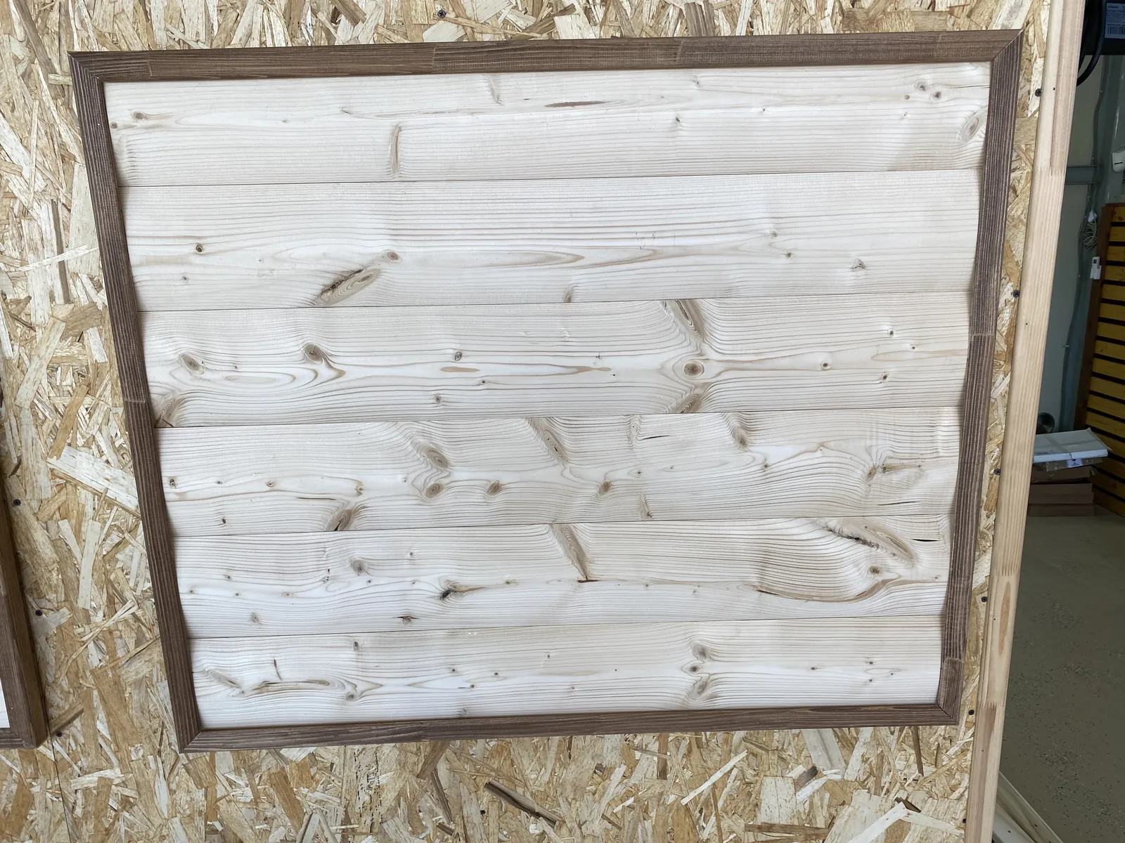 Щит из светлой доски с сучками в тёмной рамке — образец у стены из ОСП в мастерской, по нему и выбирают отделку.